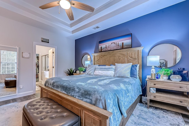 bedroom featuring hardwood / wood-style floors, a tray ceiling, ceiling fan, and ensuite bathroom