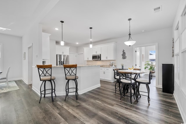 kitchen featuring dark hardwood / wood-style floors, white cabinetry, a kitchen breakfast bar, hanging light fixtures, and stainless steel appliances