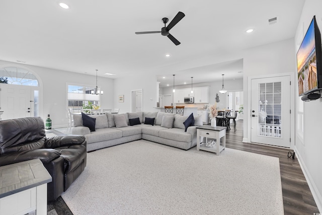 living room with ceiling fan with notable chandelier and dark wood-type flooring