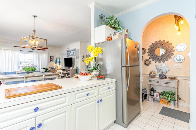 kitchen with freestanding refrigerator, light tile patterned flooring, white cabinetry, arched walkways, and a notable chandelier