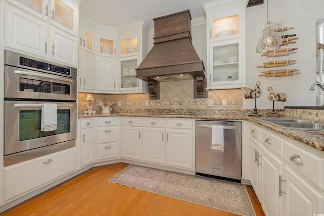 kitchen with premium range hood, sink, white cabinetry, appliances with stainless steel finishes, and light stone countertops