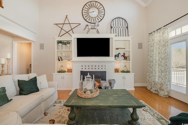 living room featuring a tiled fireplace, crown molding, a towering ceiling, and light hardwood / wood-style flooring