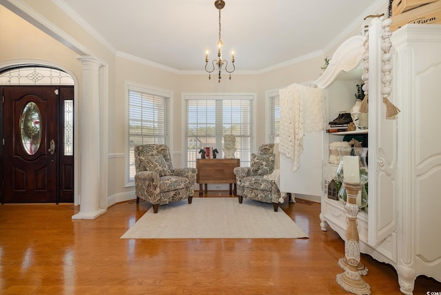 sitting room with ornate columns, wood-type flooring, ornamental molding, and a notable chandelier