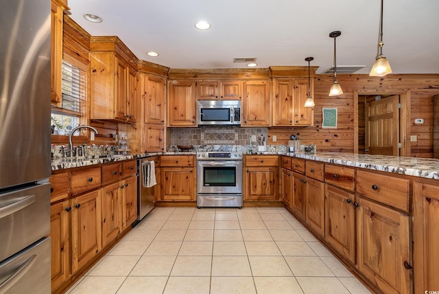 kitchen with hanging light fixtures, light tile patterned floors, appliances with stainless steel finishes, light stone countertops, and backsplash