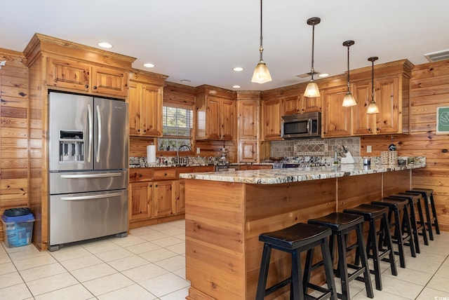 kitchen with hanging light fixtures, light tile patterned floors, light stone counters, kitchen peninsula, and stainless steel appliances