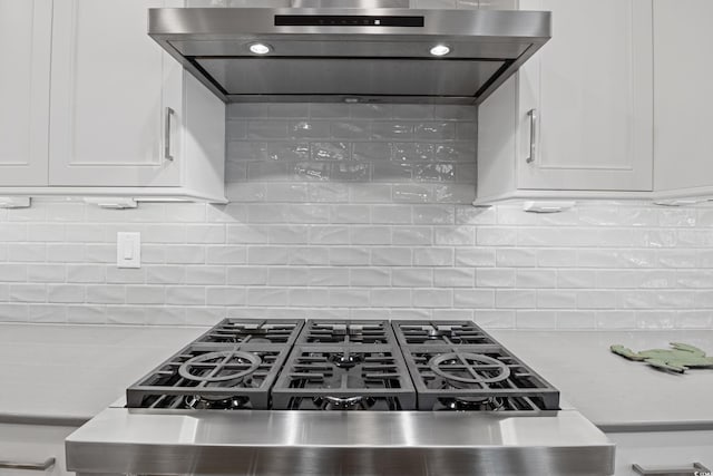 kitchen with wall chimney exhaust hood, tasteful backsplash, light countertops, and white cabinetry