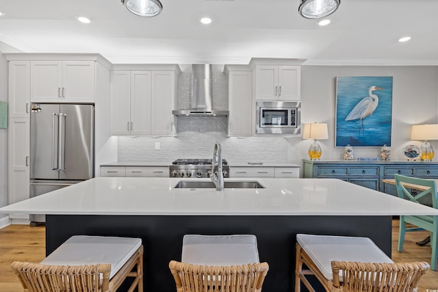 kitchen featuring wall chimney exhaust hood, appliances with stainless steel finishes, a sink, and a breakfast bar