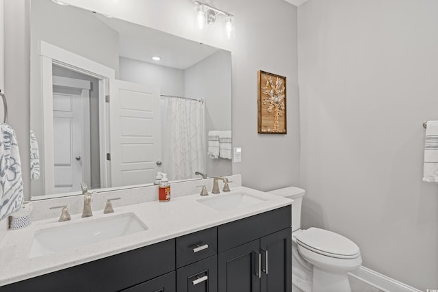 bathroom with double vanity, a sink, toilet, and baseboards