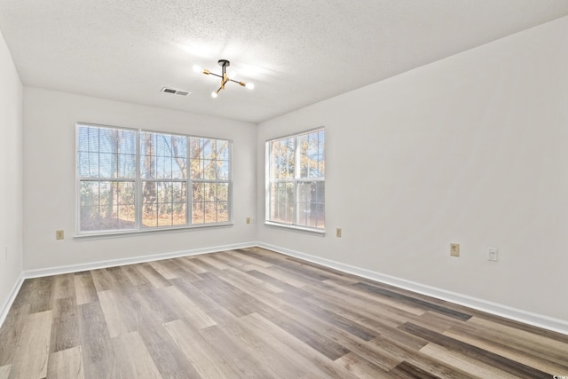 unfurnished room with an inviting chandelier, a textured ceiling, and light hardwood / wood-style floors