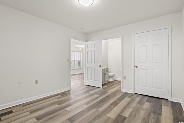 unfurnished bedroom with ensuite bath, a textured ceiling, and light wood-type flooring