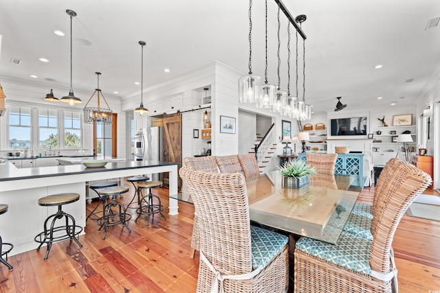 dining area featuring a notable chandelier, ornamental molding, light hardwood / wood-style floors, and a barn door