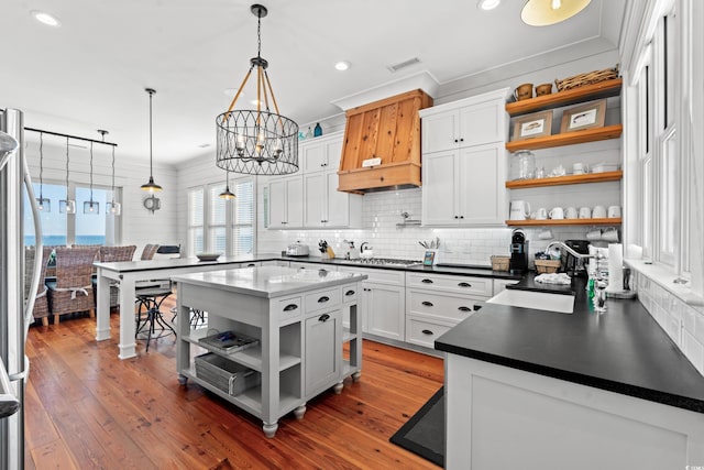 kitchen featuring dark wood-type flooring, decorative light fixtures, ornamental molding, a kitchen island, and white cabinets