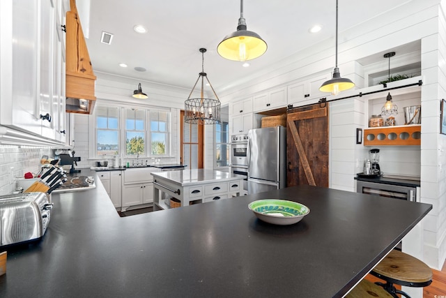 kitchen with a breakfast bar, hanging light fixtures, stainless steel appliances, white cabinets, and a barn door