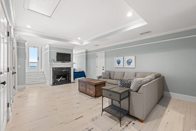 living room featuring a raised ceiling, ornamental molding, a premium fireplace, and light hardwood / wood-style flooring