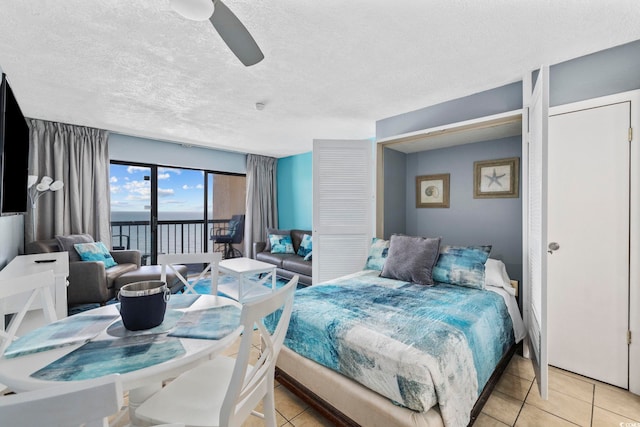 bedroom with light tile patterned floors, ceiling fan, a water view, a textured ceiling, and access to outside