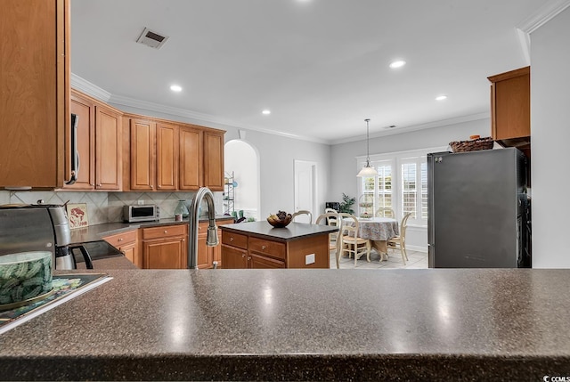 kitchen featuring crown molding, appliances with stainless steel finishes, decorative backsplash, a kitchen island, and decorative light fixtures