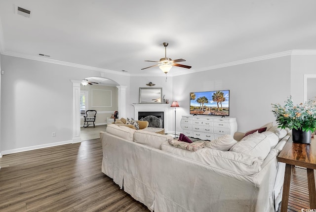 living room featuring dark wood-type flooring, ceiling fan, crown molding, and ornate columns