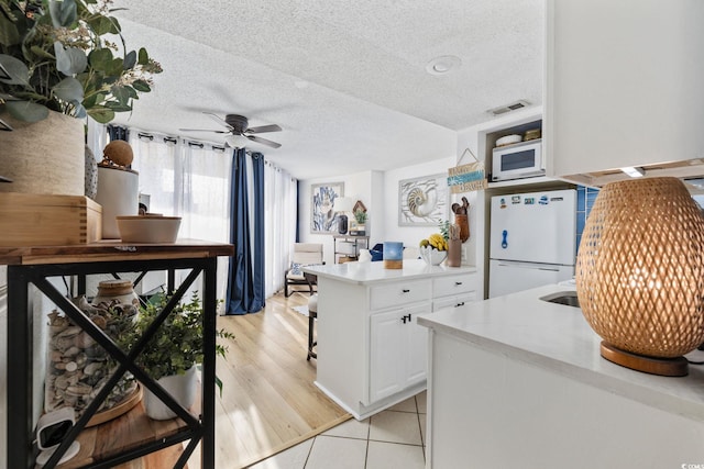 kitchen featuring white appliances, a textured ceiling, ceiling fan, light hardwood / wood-style floors, and white cabinets