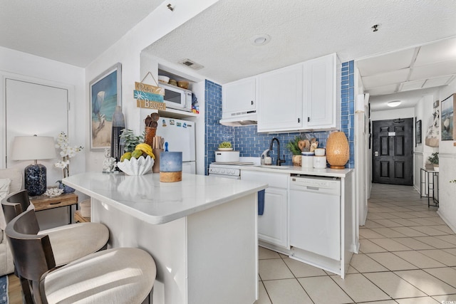 kitchen featuring a breakfast bar, white cabinetry, sink, backsplash, and white appliances