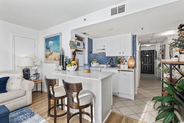 kitchen with white appliances, a breakfast bar, white cabinetry, tasteful backsplash, and kitchen peninsula