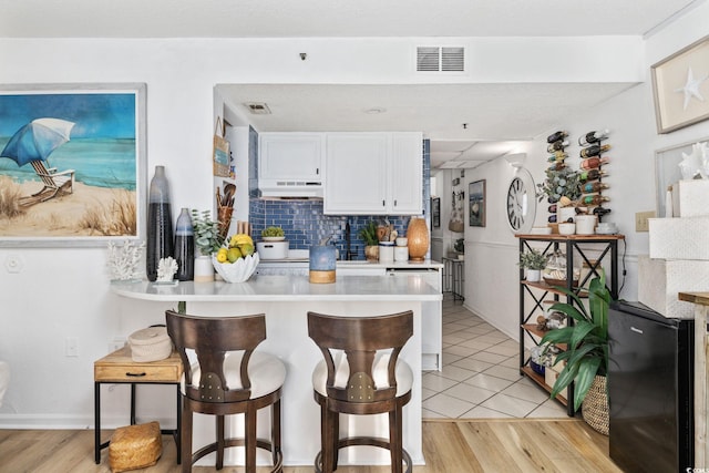 kitchen featuring white cabinetry, light hardwood / wood-style floors, a kitchen bar, and decorative backsplash