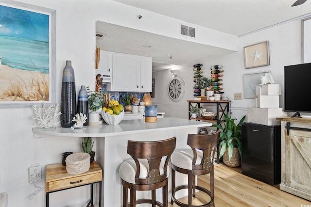 kitchen featuring a breakfast bar area, white cabinetry, a textured ceiling, light wood-type flooring, and kitchen peninsula