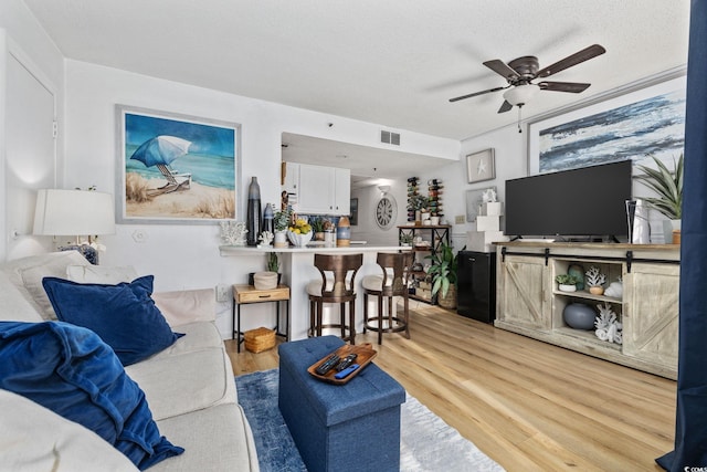 living room with ceiling fan, light hardwood / wood-style flooring, and a textured ceiling