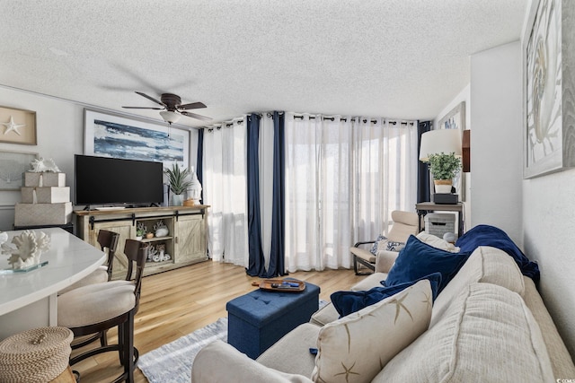 living room featuring ceiling fan, a textured ceiling, and light wood-type flooring