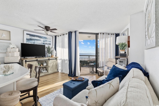 living room featuring ceiling fan, a wall of windows, light hardwood / wood-style flooring, and a textured ceiling