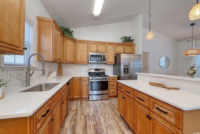 kitchen featuring vaulted ceiling, decorative light fixtures, sink, stainless steel appliances, and light hardwood / wood-style flooring