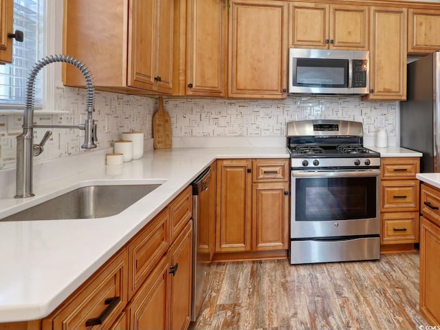 kitchen with stainless steel appliances, sink, light wood-type flooring, and decorative backsplash