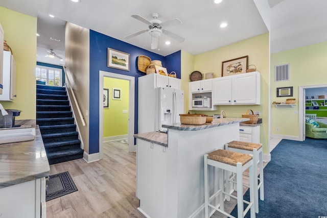 kitchen featuring white cabinetry, white fridge with ice dispenser, ceiling fan, and a kitchen breakfast bar