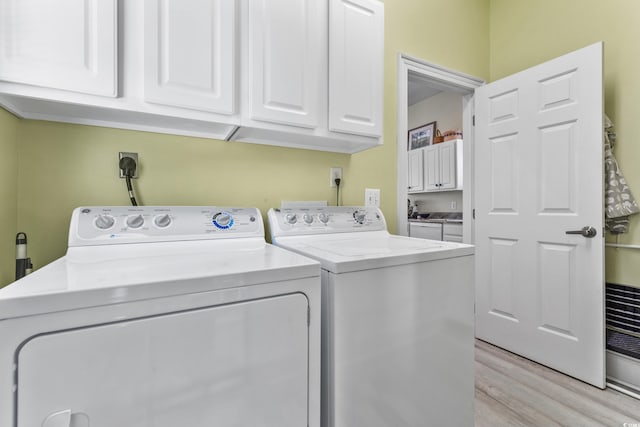 laundry room with cabinets, washer and dryer, and light hardwood / wood-style floors