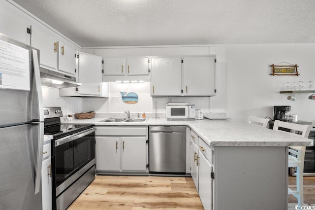 kitchen featuring a peninsula, stainless steel appliances, light wood-type flooring, under cabinet range hood, and a sink