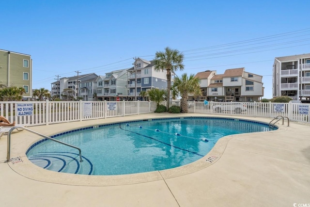 community pool with a patio area, fence, and a residential view