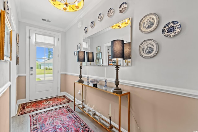 doorway with visible vents, baseboards, wood finished floors, and crown molding