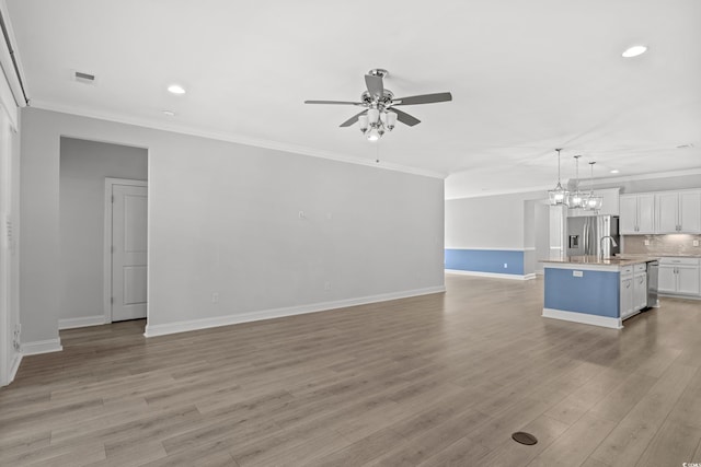 unfurnished living room featuring ceiling fan with notable chandelier, ornamental molding, sink, and light hardwood / wood-style floors