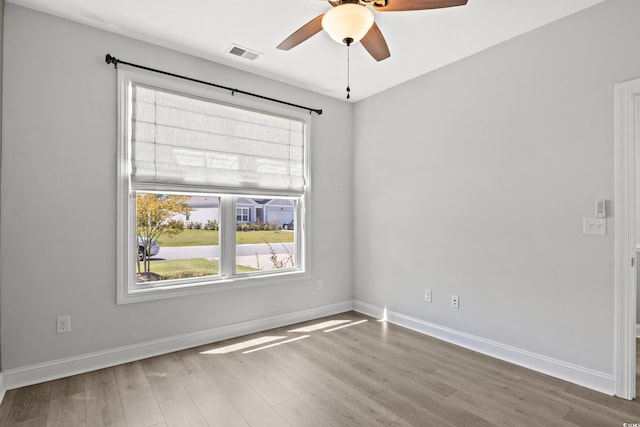 unfurnished room with a ceiling fan, wood finished floors, visible vents, and baseboards