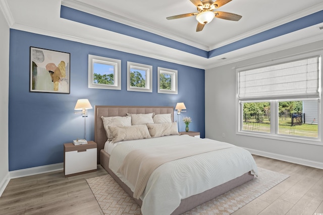 bedroom featuring light hardwood / wood-style flooring, ornamental molding, a raised ceiling, and ceiling fan