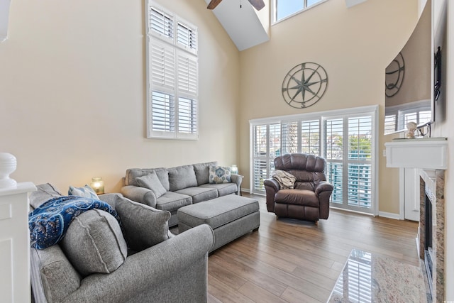 living room with light hardwood / wood-style flooring, a high end fireplace, ceiling fan, a healthy amount of sunlight, and a high ceiling