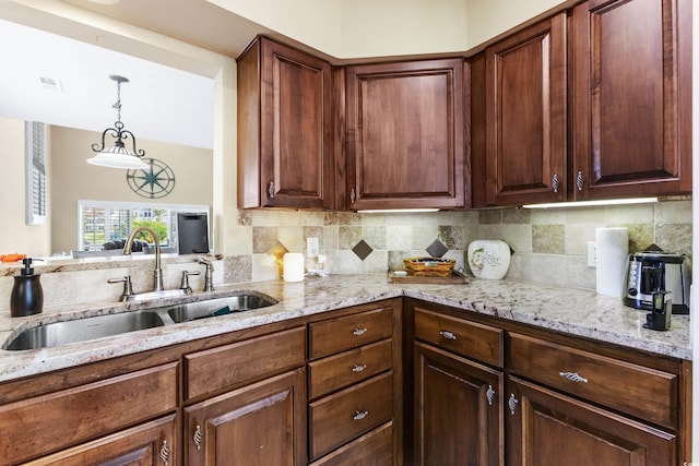 kitchen with sink, backsplash, decorative light fixtures, and light stone countertops