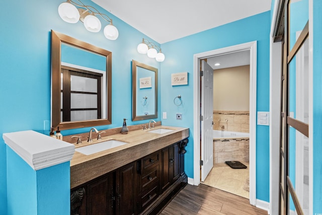 bathroom featuring hardwood / wood-style floors, vanity, and a relaxing tiled tub