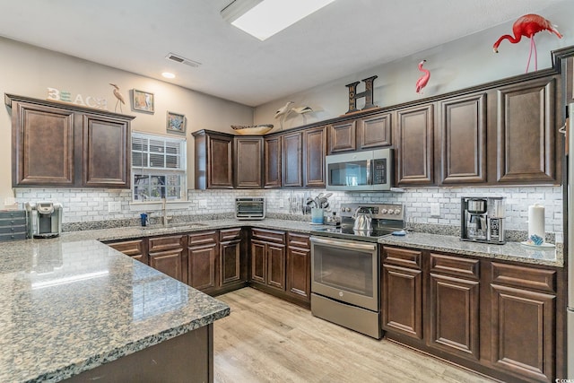 kitchen featuring sink, appliances with stainless steel finishes, dark stone countertops, tasteful backsplash, and light wood-type flooring