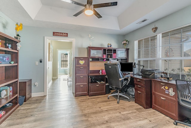 office featuring a healthy amount of sunlight, a raised ceiling, ceiling fan, and light wood-type flooring