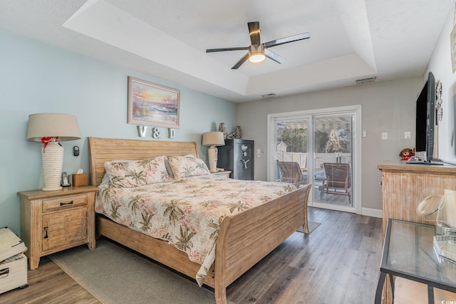 bedroom featuring ceiling fan, dark hardwood / wood-style floors, a raised ceiling, and access to outside