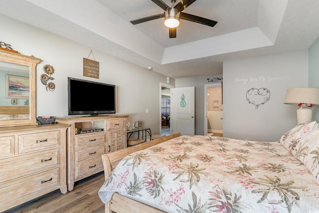 bedroom with ceiling fan, connected bathroom, light wood-type flooring, and a tray ceiling