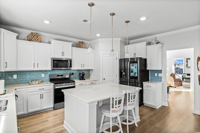 kitchen with a kitchen island, appliances with stainless steel finishes, pendant lighting, and white cabinets