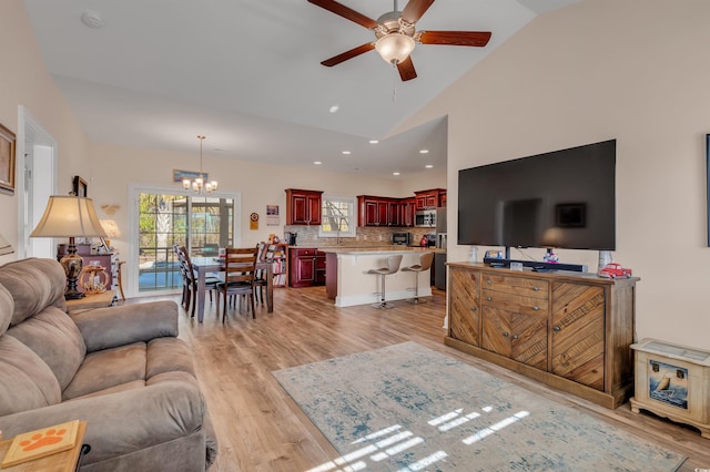 living room featuring high vaulted ceiling, ceiling fan with notable chandelier, and light hardwood / wood-style floors