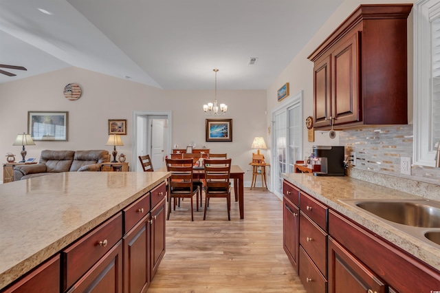 kitchen featuring lofted ceiling, tasteful backsplash, decorative light fixtures, light hardwood / wood-style flooring, and ceiling fan with notable chandelier