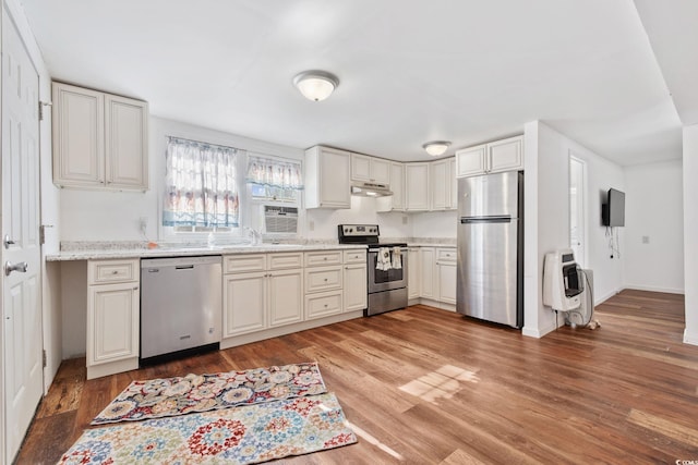 kitchen featuring stainless steel appliances, light stone countertops, white cabinets, hardwood / wood-style floors, and sink